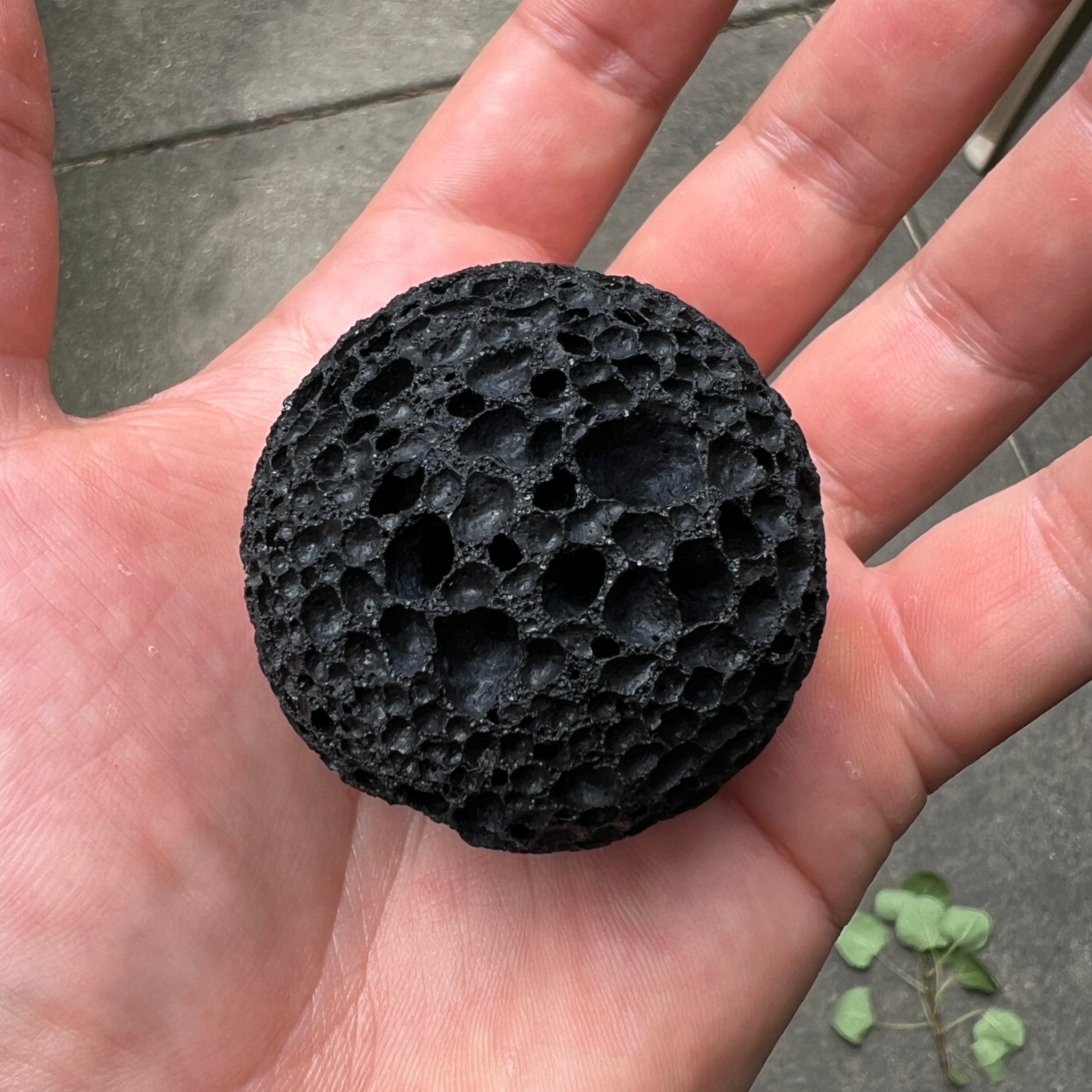 Black Komodo stone ball held in a hand with a concrete floor background
